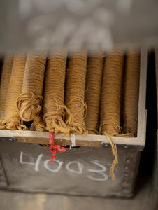 Kasthall metal box full of yellow woollen yarn bobbins wound ready for weaving.