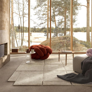 Living room with Design House Stockholm wool beige Basket rug in the centre, and a view of a natural landscape through the windows.