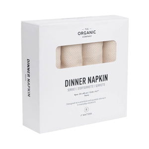 The Organic Company Stone Dinner Napkins with herringbone weave, each napkin has a looped tab sewn on for hanging. show here in its packaging, a white box with four napkins.