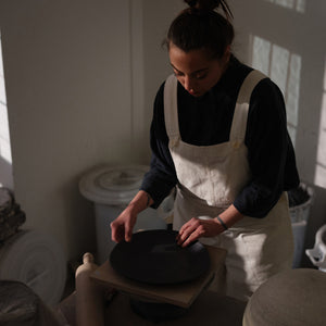 Hana Karim at work creating artisan plates with natural light casting light and shadow through the window.