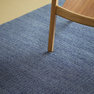 Patterned blue rug with goose eye design shown close up under wooden chair