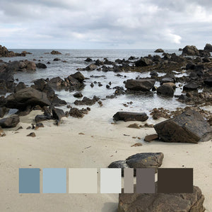 A rocky granite shoreline on a sandy beach with a sea view towards the horizon and a cloudy sky