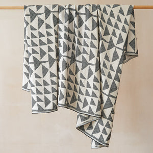 Beatrice Larkin Flint Throw in Merino wool with gentle triangle geometric pattern. Throw draped over wooden rail. 