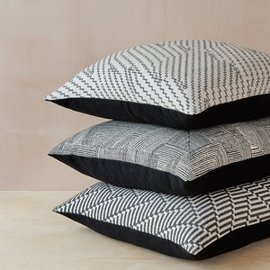Stack of three Beatrice Larkin merino wool cushions featuring a gentle monochrome geometric pattern, and plain cotton back.