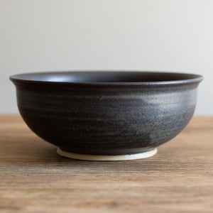 Deep ramen bowl with a softly curved rim. Hand-thrown artisan ceramic tableware handmade by Carla Murdoch in the UK. The bowl has a dramatic black glaze with golden and khaki tones. 