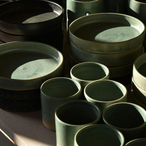 Collection of lichen green tapas dishes and stoneware tumblers a on table in sunlight. Hand-thrown artisan ceramic tableware handmade by Carla Murdoch in the UK.