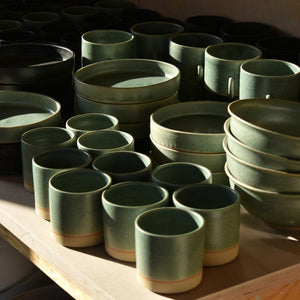 Collection of lichen green ramen bowls, tapas dishes and stoneware tumblers on a table in sunlight. Hand-thrown artisan ceramic tableware handmade by Carla Murdoch in the UK.