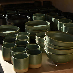 Collection of lichen green ramen bowls, tapas dishes and stoneware tumblers on table in sunlight. Hand-thrown artisan ceramic tableware handmade by Carla Murdoch in the UK.