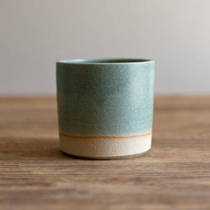 Hand-thrown artisan stoneware tumbler. Ceramic tableware handmade by Carla Murdoch in the UK. The tumbler has an earthy green lichen colour glaze. The lower section of the tumbler outer is left unglazed.