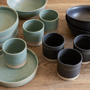Collection of deep ramen bowls with softly curved rims and stoneware tumblers on wooden table. Hand-thrown artisan ceramic tableware handmade by Carla Murdoch in the UK. 