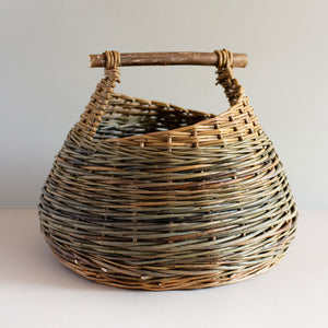 Woven willow basket with handle, handmade by basket maker Catherine Beaumont, using English grown natural willow. The willow colours vary from browns to blue-greens. The round basket has a wooden handle.