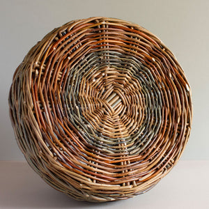 Base of a woven willow basket with handle, handmade by Catherine Beaumont basket maker. The willow colours range from russet browns to blue-greens. 
