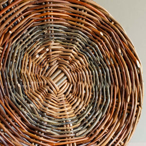 Base of a woven willow basket with handle, handmade by Catherine Beaumont basket maker. The willow colours range from russet browns to blue-greens. 