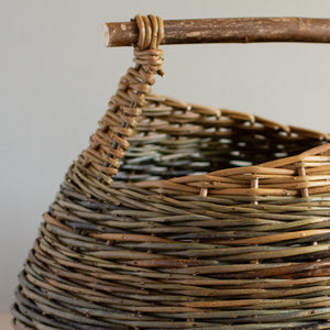 Woven willow basket with handle, handmade by basket maker Catherine Beaumont, using English grown natural willow. The willow colours vary from browns to blue-greens. The round basket has a wooden handle and an angled top edge.