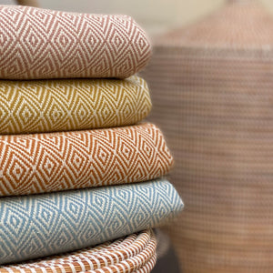 Stack of organic cotton blankets on a basket, the blankets are woven with a diamond weave pattern
