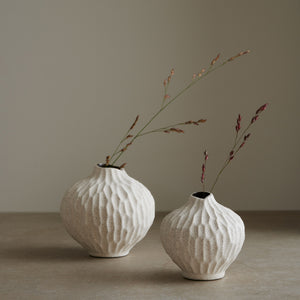 Two Lindform’s Line sand cut white bud vases with sculpted surface patterns, each displaying dried grasses