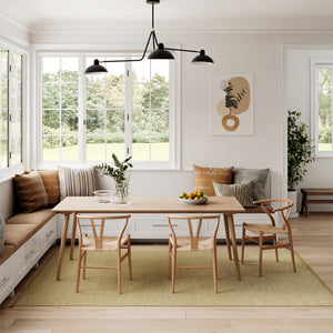 A fresh and bright kitchen dining area with bench seating in front of large white framed windows, with wooden table and chairs. A modern looking interior with Kasthall's Golden Ash Harper rug adding colour to this dining area.  Natural foliage, artwork and indoor plants add to the natural Biophilic design  decor. 