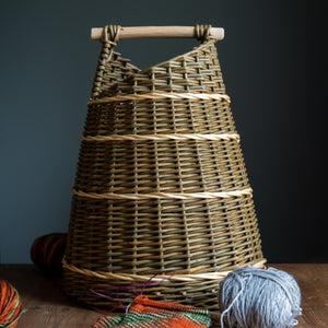 Willow asymmetric basket with white lines pictured with knitting and ball of wool. Basket handmade by Rachel Bower, photo by Manna Reid.