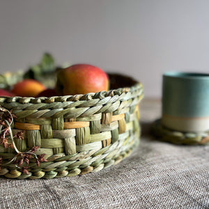 Rush Round Baskets from Rush Matters are beautifully handmade by Felicity Irons and her team in Bedfordshire, from locally harvested English bulrush. Basket of fruit with green ceramic tumbler on hemp table mat.