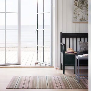 Pink and Beige striped runner by Fabula Living in a living room with french doors opening onto a beach side decking and view of the sea. 
