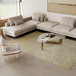 Spacious and Scandinavian style interior with large windows. Lots of natural light. Light neutral colour scheme and a wooden pitched ceiling. Kasthall’s Early Spring Greta rug is placed in front of a large beige modular sofa and under a designer coffee table. The rug's colours are a refreshing mix of beige neutrals and cream with green, lemon and ochre hues.