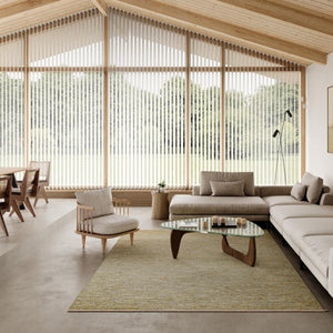 Spacious and Scandinavian style interior with large windows overlooking a garden and trees. Lots of natural light. Light neutral colour scheme and a wooden pitched ceiling.  Kasthall’s Early Spring Greta rug is placed under a designer coffee table. The rug's colours are a refreshing mix of beige neutrals and cream with green, lemon and ochre hues.