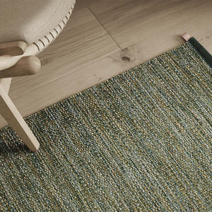 Kasthall's summer breeze Greta rug mixes greens, beiges, blue and lime hues - shown close up under armchair. 