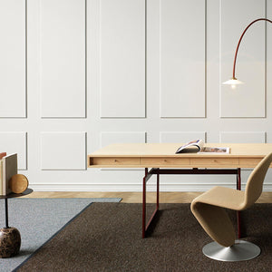 Kasthall’s Terrazzo rug is a woven bouclé rug in pure wool and linen. A mix of colours and fibres are woven together to create a wonderfully textured surface. Two rugs overlap each other in front of white wall panels. There is a pale wooden desk and curved chair on the brown rug and an arced red lamp overhead. 