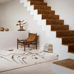 Knots Rugs charcoal shadow rug in living area with brown leather armchair, natural decor, white walls and wooden staircase.