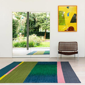 Gelim rug by Ptolemy Mann with an ikat stripe design in room with a large window looking onto a garden.