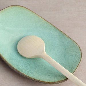 Green glazed handmade ceramic Hana Karim plate with an unglaze grey clay rim, with a wooden spoon.