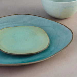 Avo green and blue lagoon glazed handmade ceramic Hana Karim plates stacked together on table.