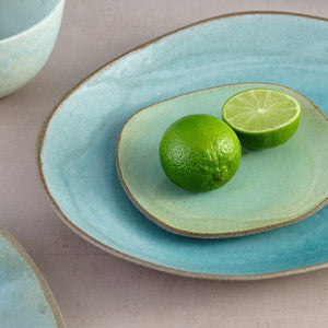 Avo green and blue lagoon glazed handmade ceramic Hana Karim plates stacked together on table, with a lime fruit garnish.