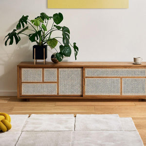 Living room with Design House Stockholm wool beige Basket rug in front of a wooden rattan sideboard with house plant on the sideboard and yellow cushion on the rug.