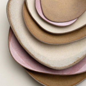 Hana Karim stoneware plates and serving platters stacked together showing a colour palette of pinks, beige and honey brown.