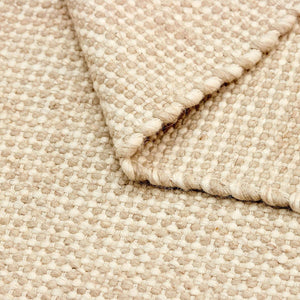 Close up of the Beige Nordic Touch Rug by Rezas is a handwoven kelim. The inviting texture is crafted by weaving together varied yarn weights in beige and cream hues. Natural variations in the yarn tones brings added character to the design.