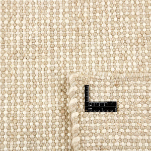 Close up of the Beige Nordic Touch Rug by Rezas is a handwoven kelim. The inviting texture is crafted by weaving together varied yarn weights in beige and cream hues. Natural variations in the yarn tones brings added character to the design. Ruler in image for scale.