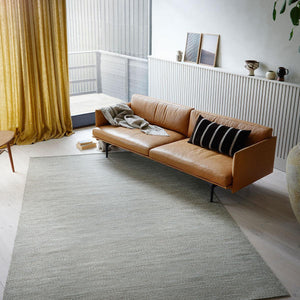 The Fabula Living’s Beige/Grey Gimle Rug on the floor in a light coloured room, with a tan leather sofa positioned across the corner of the rug - designed by Jens Landberg Schrøder