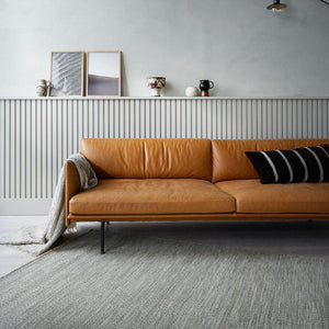 The Fabula Living’s Beige/Grey Gimle Rug on the floor in a light coloured room, with a tan leather sofa positioned across the corner of the rug - designed by Jens Landberg Schrøder