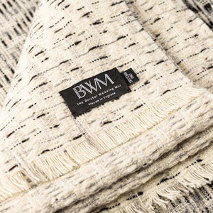The Bristol Weaving Mill Wool and Linen Blanket in black and grey is folded with the corner turned back to show the brand and care labels.. 