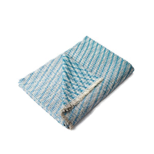 The Bristol Weaving Mill Wool and Linen Blanket in blue and teal is folded with the corner turned back to show the complex diagonal weave pattern. 