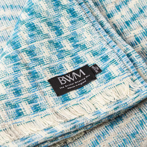 The Bristol Weaving Mill Wool and Linen Blanket in blue and teal is folded with the corner turned back to show the brand and care label.