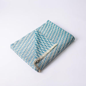 The Bristol Weaving Mill Wool and Linen Blanket in blue and teal is folded with the corner turned back to show the complex diagonal weave pattern. 