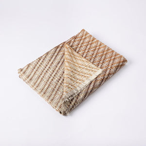 The Bristol Weaving Mill Wool and Linen Blanket in earthy brown tones is folded with the corner turned back to show the complex diagonal, criss-cross, weave pattern. 