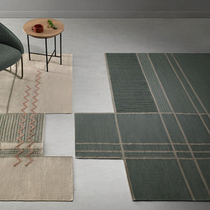 Tacto's Caminos Green Rug in a light room alongside a cream rug, armchair and side table  - designed by Yonoh.