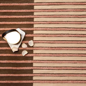 A close up look at Tacto's Campos Blush Rug, this linear, textured and tonal striped rug is handwoven with an 8 mm wool pile. Colours graduate from rich earthy brown to blush pink - designed by Aranda Aloy Enblanc.