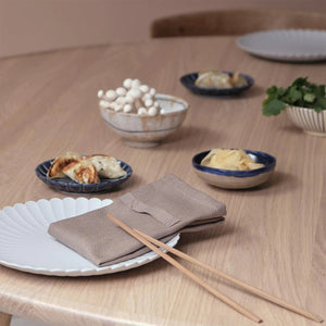 The Organic Company Clay Dinner Napkin folded on a plate with chopsticks resting on the napkin and alongside are dishes of food.