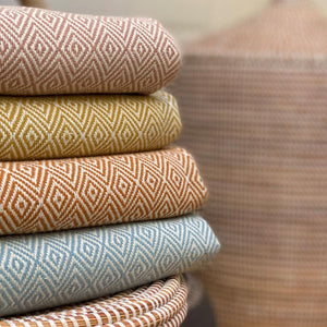 full colour range of Damla organic cotton blankets by Lüks. With a diamond pattern. shown in stack of four folded blankets on a box. 