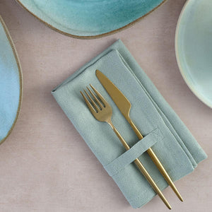 The Organic Company cotton cloth napkin neatly folded with a knife and fork placed on it, on a table set with serving plates.