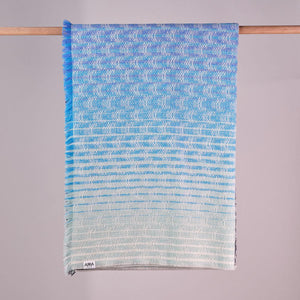 Arra Textiles, nature inspired woven blanket in blue aqua tones, hanging on wooden pole.